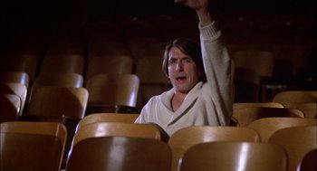 Movie still from “Teen Wolf” (1985), directed by Rod Daniel – A man sitting in an empty theater with his arms raised; Medium shot, Low angle