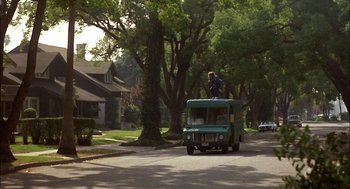 Movie still from “Teen Wolf” (1985), directed by Rod Daniel – A man standing on the roof of a bus on the road; Extreme Wide shot, Low angle