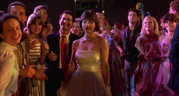 Movie still from “Teen Wolf” (1985), directed by Rod Daniel – A woman in a white dress standing in front of a group of people; Medium shot, Low angle