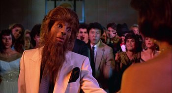 Movie still from “Teen Wolf” (1985), directed by Rod Daniel – A group of people in a crowd with a man in a werewolf mask; Medium shot, Over the shoulder angle