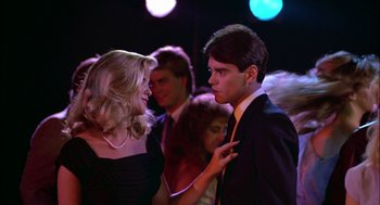 Movie still from “Teen Wolf” (1985), directed by Rod Daniel – A man and a woman are talking in front of a crowd; Medium shot, Over the shoulder angle