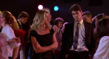 Movie still from “Teen Wolf” (1985), directed by Rod Daniel – A man and a woman are standing in front of other people; Medium shot, Low angle