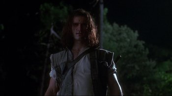 Movie still from “Teenage Mutant Ninja Turtles” (1990), directed by Steve Barron – A man with long dark hair is standing in the dark; Medium shot, Low angle
