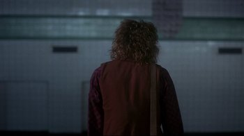 Movie still from “Teenage Mutant Ninja Turtles” (1990), directed by Steve Barron – A person with curly hair is standing in the dark; Wide shot, Over the shoulder angle