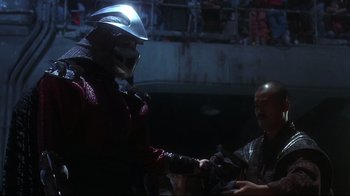 Movie still from “Teenage Mutant Ninja Turtles” (1990), directed by Steve Barron – A man wearing a helmet is shaking hands with another man; Medium shot, Over the shoulder angle