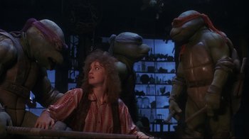 Movie still from “Teenage Mutant Ninja Turtles” (1990), directed by Steve Barron – A woman sitting at a table in front of a group of turtles; Medium shot, Over the shoulder angle