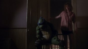 Movie still from “Teenage Mutant Ninja Turtles” (1990), directed by Steve Barron – A teenage mutant ninja turtle sitting in front of a woman; Medium shot, Low angle