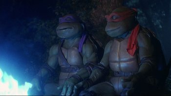 Movie still from “Teenage Mutant Ninja Turtles” (1990), directed by Steve Barron – A couple of teenage mutant ninja turtles sitting next to each other; Medium shot, Low angle