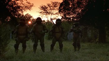 Movie still from “Teenage Mutant Ninja Turtles” (1990), directed by Steve Barron – A group of men in full body suits standing in a field; Wide shot, Low angle
