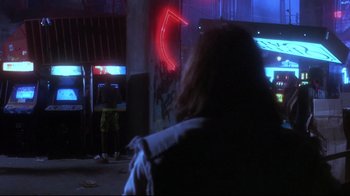 Movie still from “Teenage Mutant Ninja Turtles” (1990), directed by Steve Barron – A woman standing next to a wall in a dark room; Wide shot, Over the shoulder angle