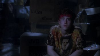 Movie still from “Teenage Mutant Ninja Turtles” (1990), directed by Steve Barron – A young man sitting in a dark room with boxes; Medium shot, Over the shoulder angle