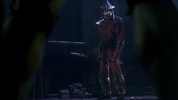 Movie still from “Teenage Mutant Ninja Turtles” (1990), directed by Steve Barron – A man in a red outfit and a hat holding a sword; Wide shot, Low angle