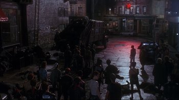 Movie still from “Teenage Mutant Ninja Turtles” (1990), directed by Steve Barron – A group of people sitting on the ground near a dump truck; Extreme Wide shot, High angle