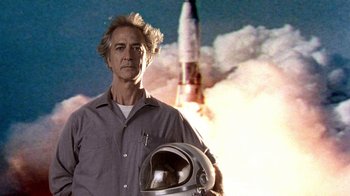 A man wearing a space helmet standing in front of a rocket