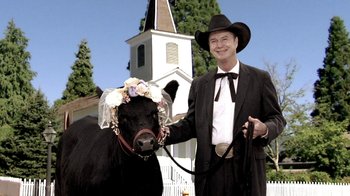 Movie still from “Temple Grandin” (2010), directed by Mick Jackson – A man in a black suit and a hat is holding a black cow; Medium shot, Low angle