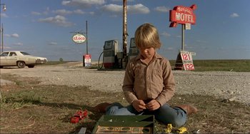 Movie still from “Tender Mercies” (1983), directed by Bruce Beresford – A young boy sitting on the ground next to an open suitcase; Wide shot, Low angle