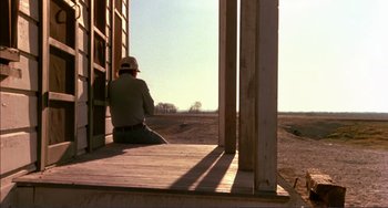 Movie still from “Tender Mercies” (1983), directed by Bruce Beresford – A man sitting on the porch of a house; Wide shot, Low angle