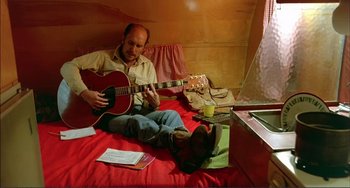 Movie still from “Tender Mercies” (1983), directed by Bruce Beresford – A man sitting on a bed playing a guitar; Medium shot, High angle