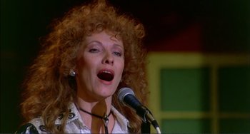 Movie still from “Tender Mercies” (1983), directed by Bruce Beresford – A woman with curly hair is singing into a microphone; Close Up shot, Low angle