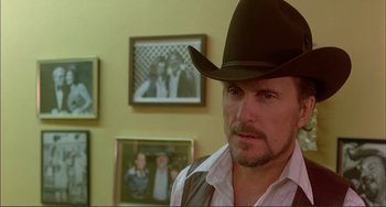 Movie still from “Tender Mercies” (1983), directed by Bruce Beresford – A man wearing a cowboy hat in front of pictures; Close Up shot, Over the shoulder angle