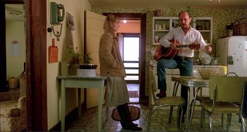 Movie still from “Tender Mercies” (1983), directed by Bruce Beresford – A man and a woman sitting at a table playing a guitar; Wide shot, Low angle