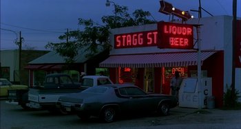 Movie still from “Tender Mercies” (1983), directed by Bruce Beresford – A car parked in front of a liquor store at night; Wide shot, High angle