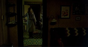 Movie still from “Tender Mercies” (1983), directed by Bruce Beresford – A woman standing in a dark room with a lamp; Wide shot, High angle