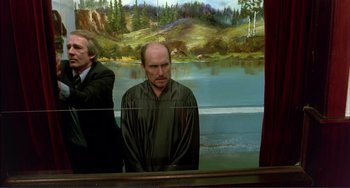 Movie still from “Tender Mercies” (1983), directed by Bruce Beresford – A man standing in front of a painting of a lake; Medium shot, Over the shoulder angle