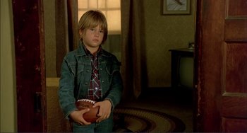 Movie still from “Tender Mercies” (1983), directed by Bruce Beresford – A young boy holding a football in a room; Medium shot, High angle