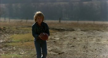 Movie still from “Tender Mercies” (1983), directed by Bruce Beresford – A young boy holding a football in a field; Wide shot, Low angle