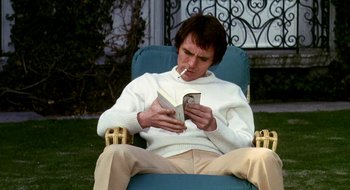 Movie still from “Teorema” (1968), directed by Pier Paolo Pasolini – A man sitting in a chair smoking a cigarette and reading a book; Medium shot, High angle