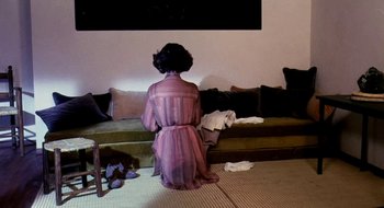 Movie still from “Teorema” (1968), directed by Pier Paolo Pasolini – A woman sitting on the ground in front of a couch; Medium shot, High angle