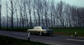 Movie still from “Teorema” (1968), directed by Pier Paolo Pasolini – A car driving down a road near a forest; Wide shot, Low angle