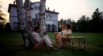 Movie still from “Teorema” (1968), directed by Pier Paolo Pasolini – A man and a woman sitting on a lawn next to a tree; Wide shot, Low angle