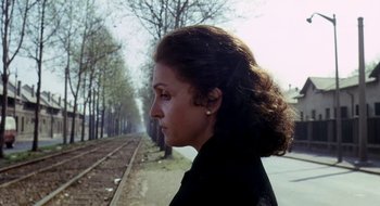 Movie still from “Teorema” (1968), directed by Pier Paolo Pasolini – A young woman with long dark curly hair is standing on the side of a train track; Close Up shot, Over the shoulder angle