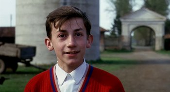 Movie still from “Teorema” (1968), directed by Pier Paolo Pasolini – A young man wearing a red sweater standing in a yard; Close Up shot, Low angle