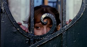 Movie still from “Teorema” (1968), directed by Pier Paolo Pasolini – A woman peeking through a metal gate with a spiraling design on it's side; Close Up shot, High angle