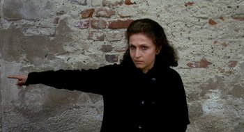Movie still from “Teorema” (1968), directed by Pier Paolo Pasolini – A woman in a black jacket standing in front of a brick wall; Medium shot, High angle