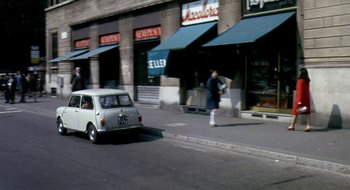 Movie still from “Teorema” (1968), directed by Pier Paolo Pasolini – A white car driving down a street next to shops; Wide shot, High angle