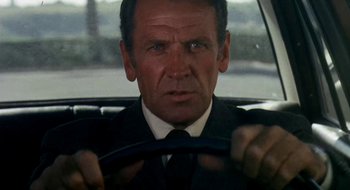 Movie still from “Teorema” (1968), directed by Pier Paolo Pasolini – A man wearing a suit and tie driving a car; Close Up shot, Low angle