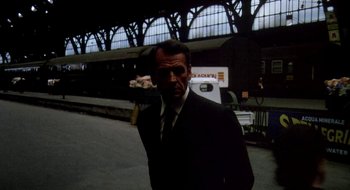 Movie still from “Teorema” (1968), directed by Pier Paolo Pasolini – A man wearing a suit and tie standing in front of a train; Medium shot, Over the shoulder angle