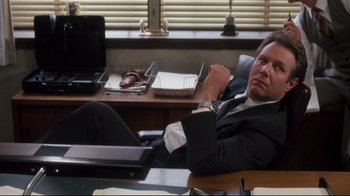 Movie still from “Tequila Sunrise” (1988), directed by Robert Towne – A man sitting at a desk in a suit; Medium shot, Low angle