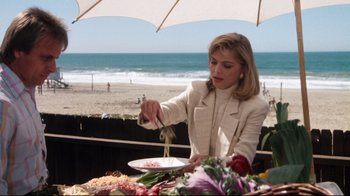 Movie still from “Tequila Sunrise” (1988), directed by Robert Towne – A woman in a white jacket is cutting food on a plate; Medium shot, Over the shoulder angle