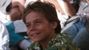 Movie still from “Tequila Sunrise” (1988), directed by Robert Towne – A young boy smiling for the camera while sitting in a crowd; Close Up shot, Low angle