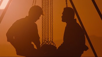 Movie still from “Tequila Sunrise” (1988), directed by Robert Towne – Two men sitting in front of each other in front of a chain link fence; Wide shot, Over the shoulder angle
