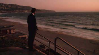 Movie still from “Tequila Sunrise” (1988), directed by Robert Towne – A man in a suit standing on a railing looking out at the ocean; Wide shot, High angle