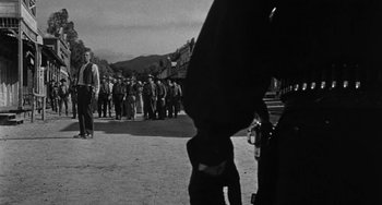 Movie still from “Terror in a Texas Town” (1958), directed by Joseph H. Lewis – Black and white photograph of people standing on a street; Wide shot, Over the shoulder angle