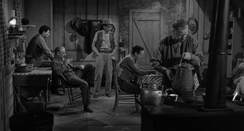 Movie still from “Terror in a Texas Town” (1958), directed by Joseph H. Lewis – A black and white photo of a group of men sitting around a table; Wide shot, High angle
