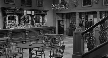 Movie still from “Terror in a Texas Town” (1958), directed by Joseph H. Lewis – A man standing in a room next to a bar; Wide shot, Over the shoulder angle