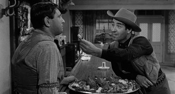 Movie still from “Terror in a Texas Town” (1958), directed by Joseph H. Lewis – A man in a cowboy hat is holding a plate of food; Medium shot, Over the shoulder angle